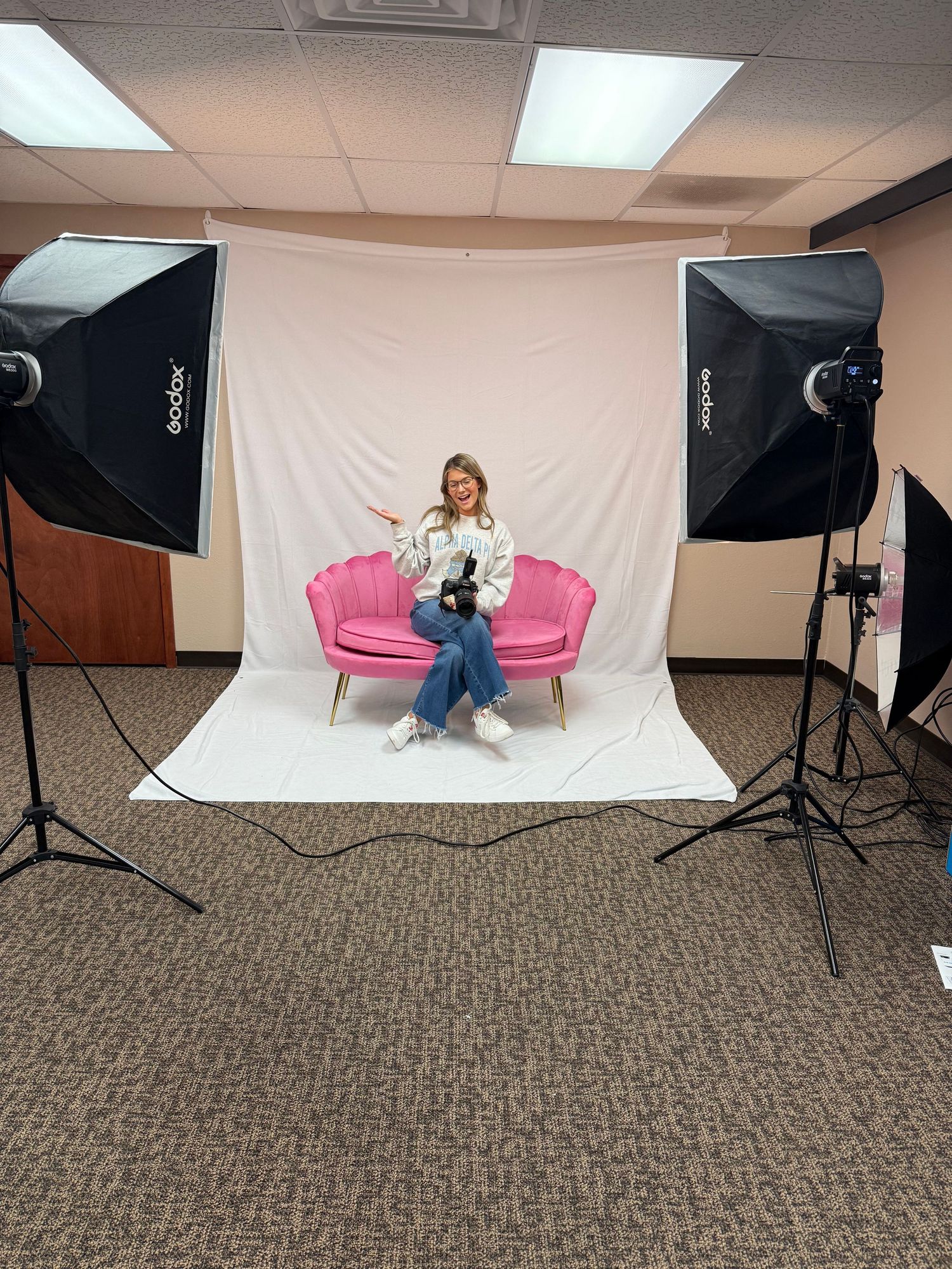 Professional photo studio setup showing lighting equipment, white backdrop, and pink chairs arranged for portrait photography.
