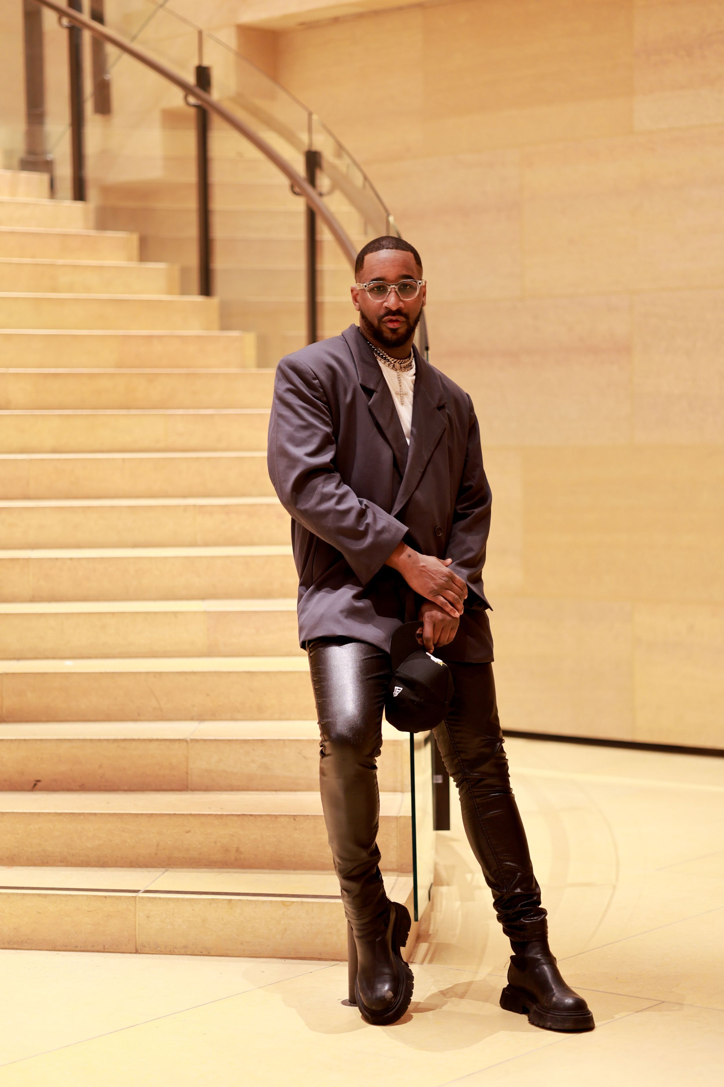A person in a stylish black blazer and leather pants poses on marble stairs with chunky boots.