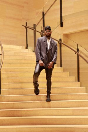 A person in a gray suit and hat descends a series of light wooden stairs in a sequential photo collage.
