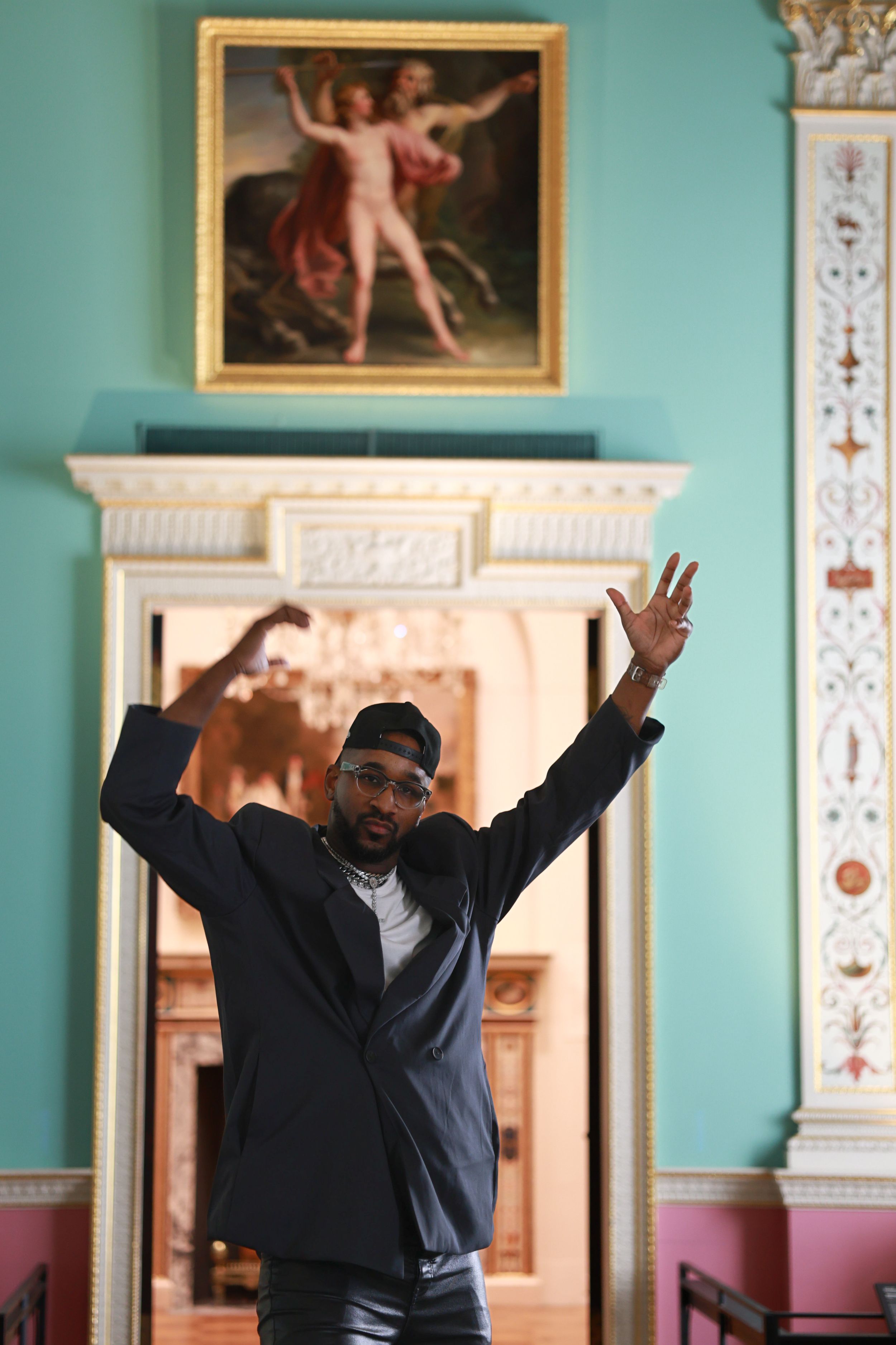 A person in a dark sweater raises their arms joyfully in an elegant room with turquoise walls and ornate decor.