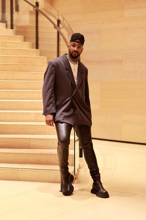 Modern fashion look with dark blazer, leather pants and combat boots photographed on beige staircase.