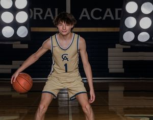 Cathedral Academy basketball player in a gold jersey dribbling on a dark indoor court with spotlights in Charleston South Carolina
