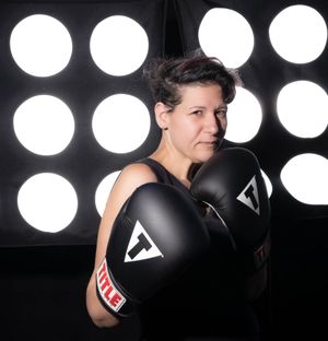 Athletic woman posing with black boxing gloves against circular light backdrop at Title Boxing Gym in Summerville South Carolina