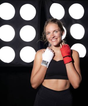 Fitness athlete in black sports top posing with boxing gloves against circular lights at Title Boxing Gym in Summerville South Carolina