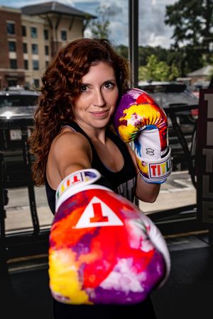 Athlete modeling colorful tie dye boxing gloves at Title Boxing Gym against a brick building in Summerville South Carolina