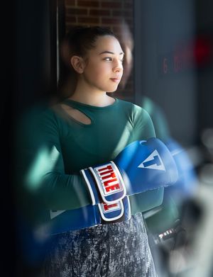 Woman in teal shirt practicing a posing out a window with blue and red gloves at Title Boxing Gym in Summerville South Carolina
