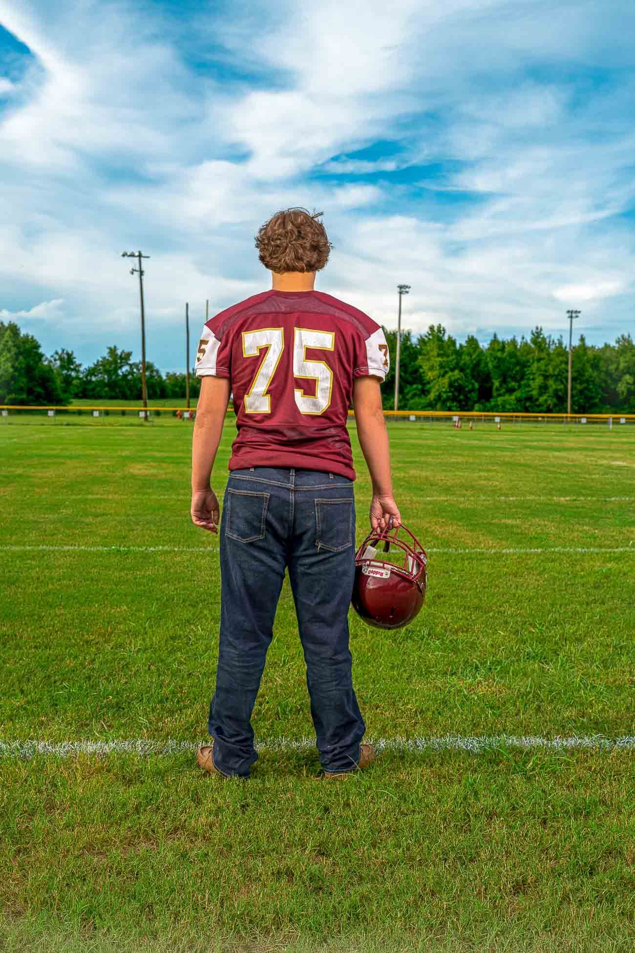 Dorchester Academy football player in a maroon jersey holding a football on a field under blue summer skies in St George South Carolina