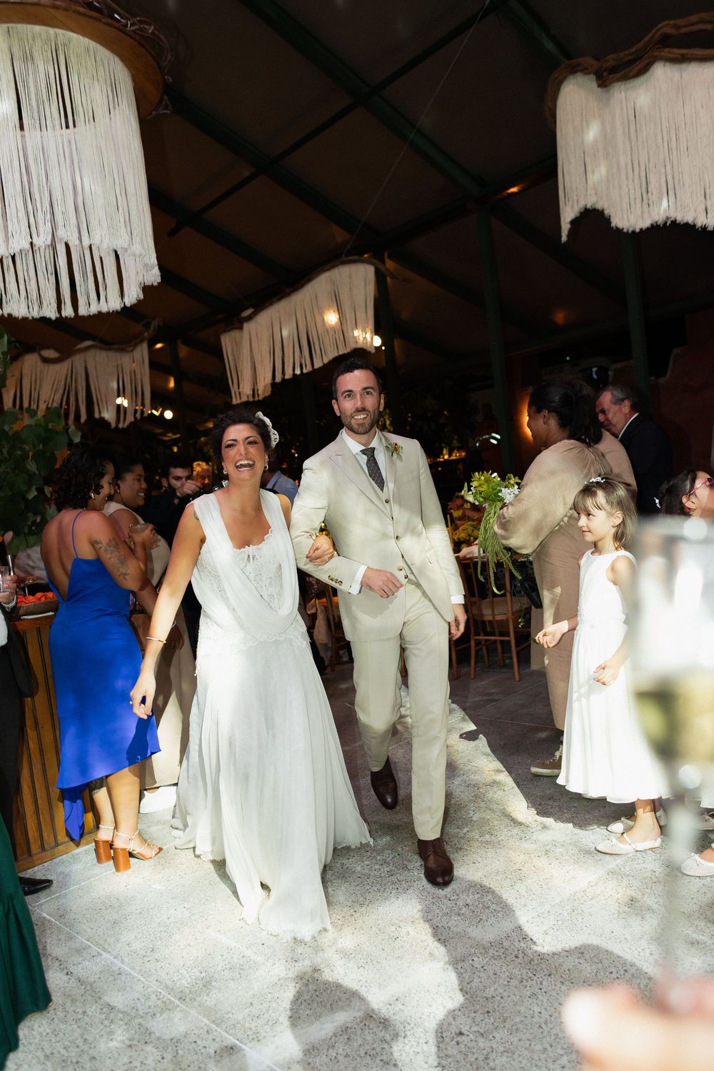 Wedding guests in white attire dance and celebrate on a decorated dance floor with hanging decorations.
