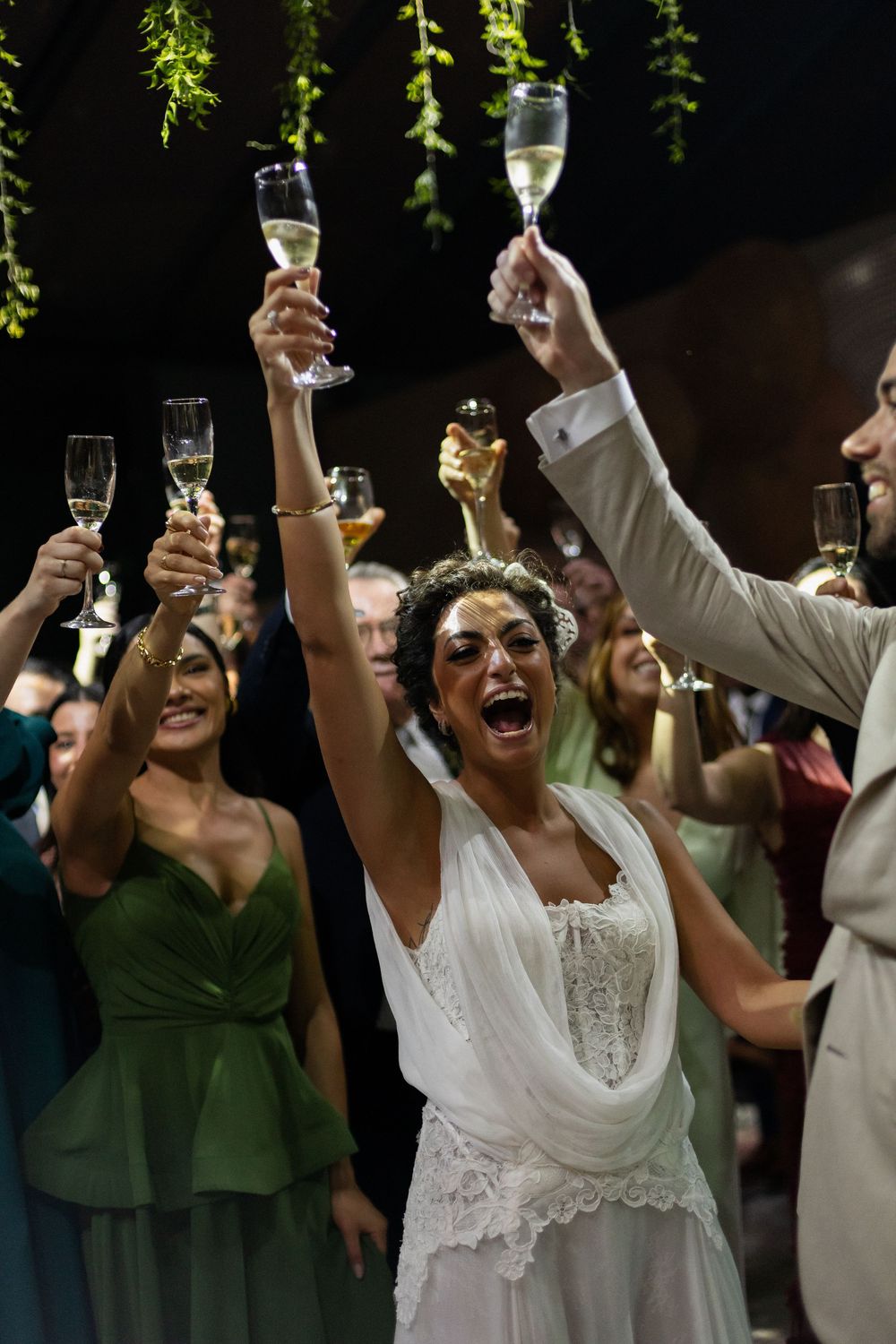 A group of wedding guests raise their champagne glasses in celebration during a joyful outdoor toast.