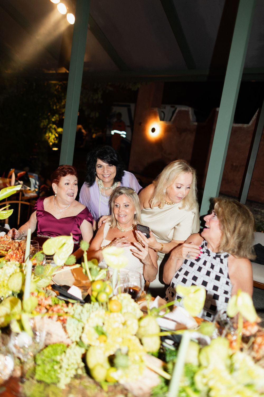 Guests gather around an elegantly decorated dinner table with floral centerpieces and ambient lighting at an evening event.