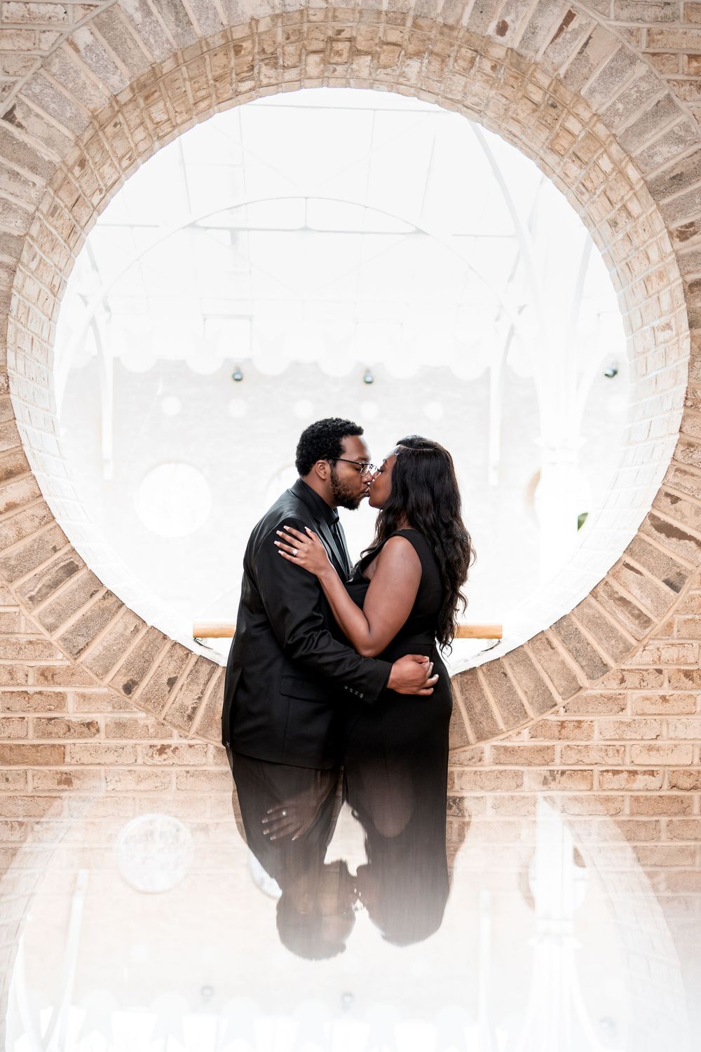 A couple shares a romantic moment framed within a circular brick archway.
