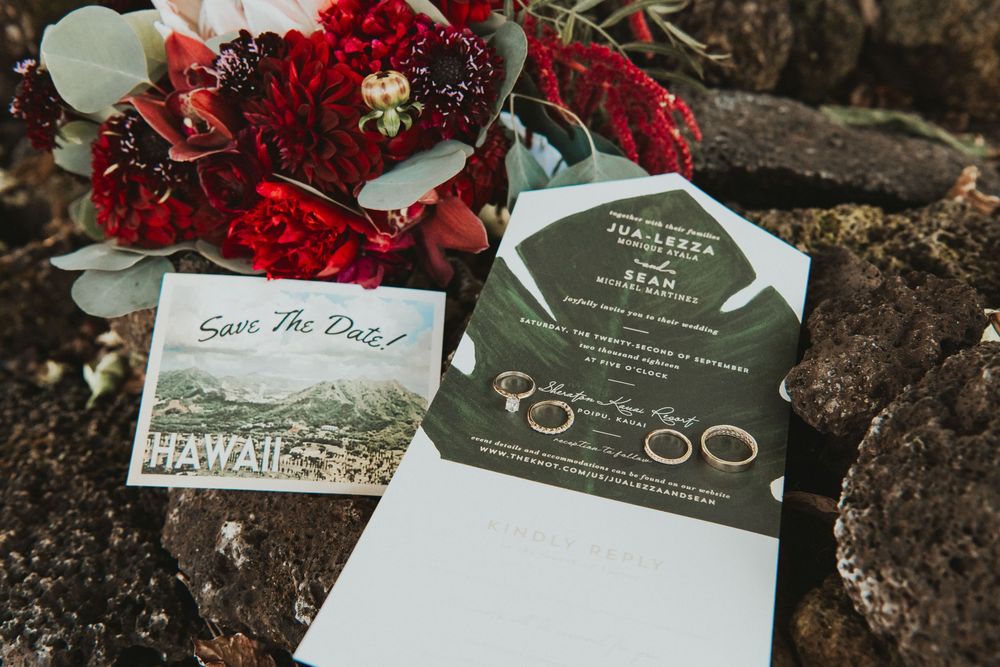 Hawaii wedding stationery with save the date card, green invitation, rings, and red floral bouquet.