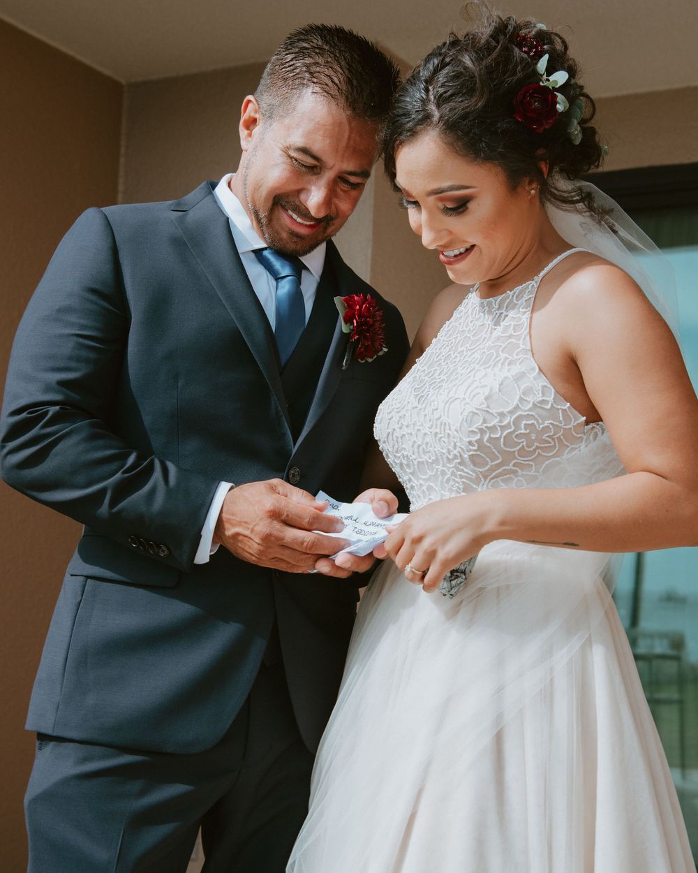Smiling bride and groom in navy suit share a tender moment exchanging a small gift together.
