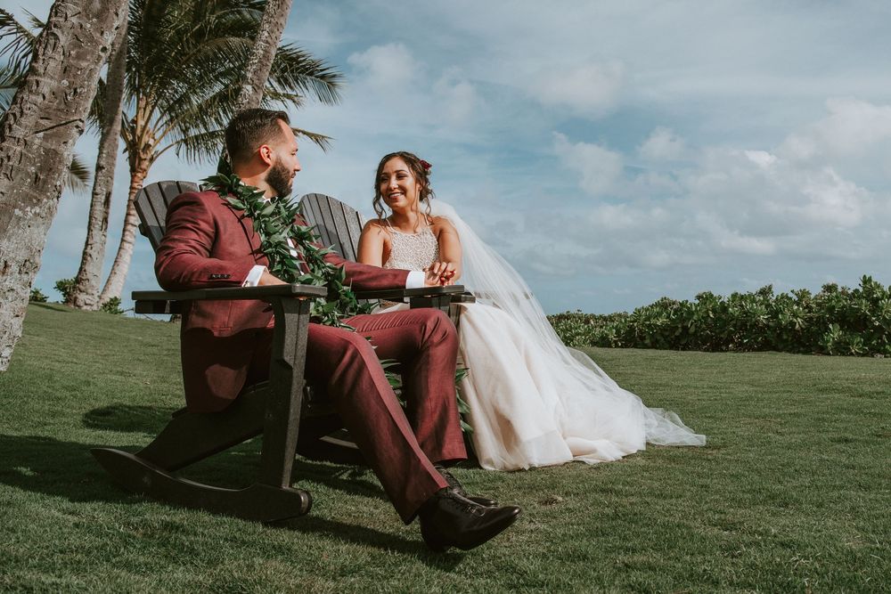 Bride and groom sit together on lawn chairs reading vows at tropical Hawaii wedding.
