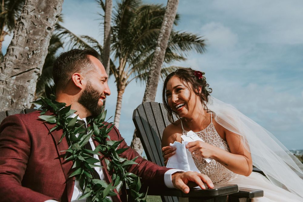 Laughing bride and groom in burgundy suit enjoy joyful moment at tropical Hawaii wedding.
