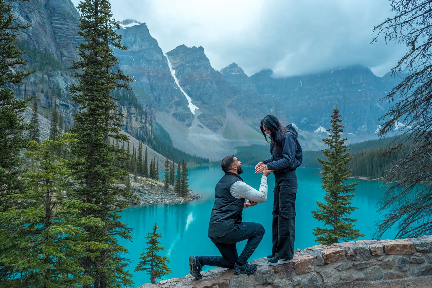 A romantic proposal moment at Moraine Lake in Banff National Park with turquoise waters and mountain peaks in background.
