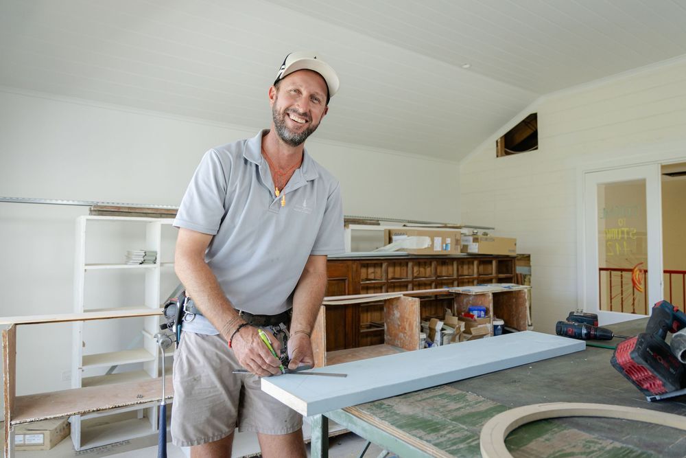 Carpenter working on installing decorative wood trim and molding in a bright white interior space.