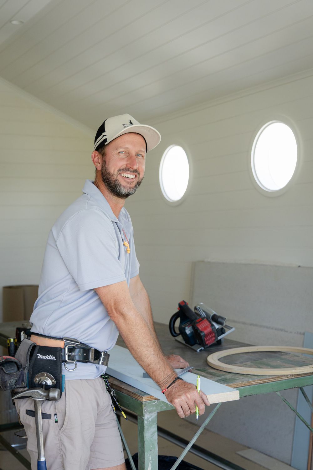 Carpenter working at bench station with power tools near circular windows in bright room Kirsten Graham Photography