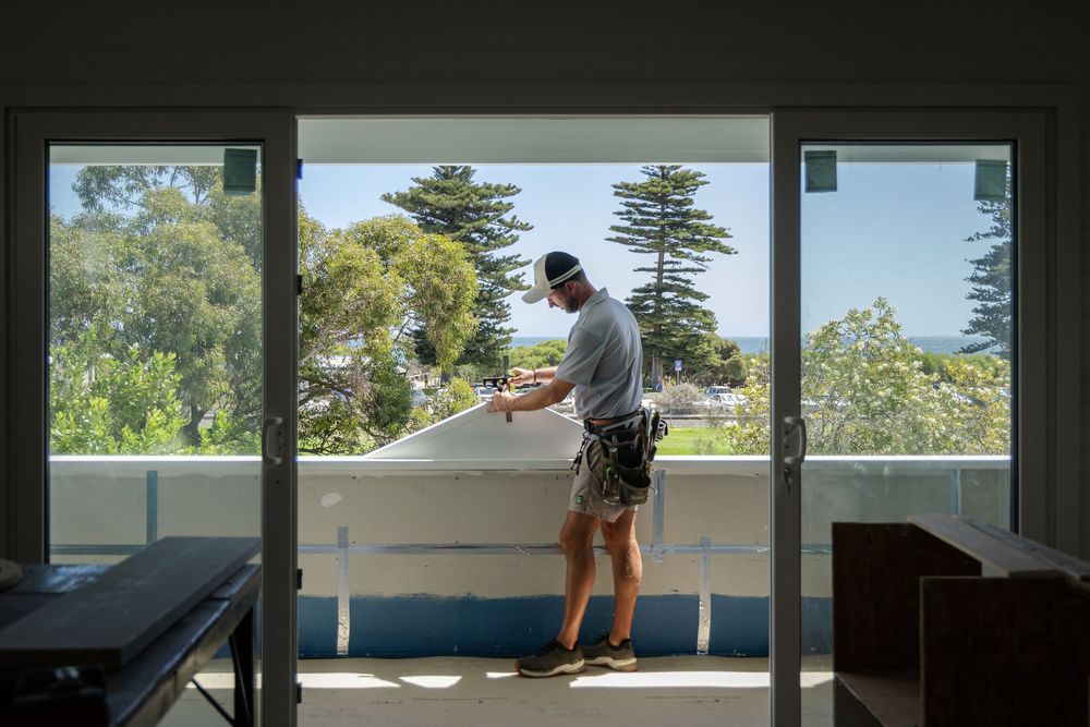 Branding photography carpenter working on a balcony with trees visible in the background.