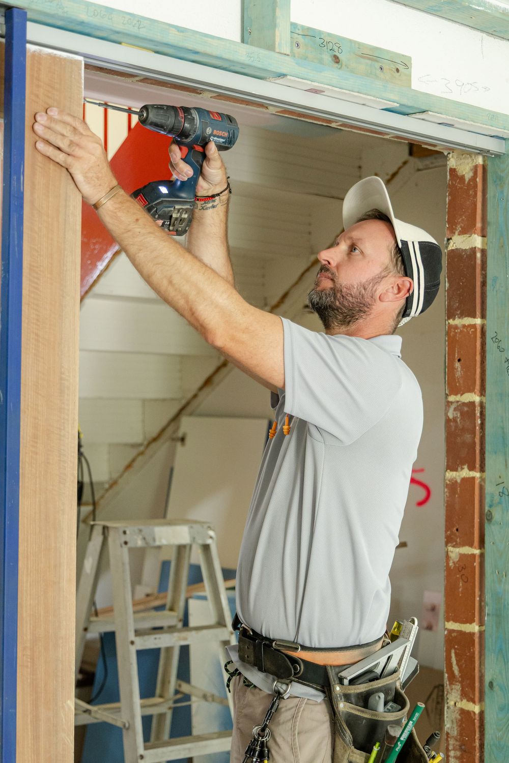 Construction worker using power drill to install framing in doorway during renovation.