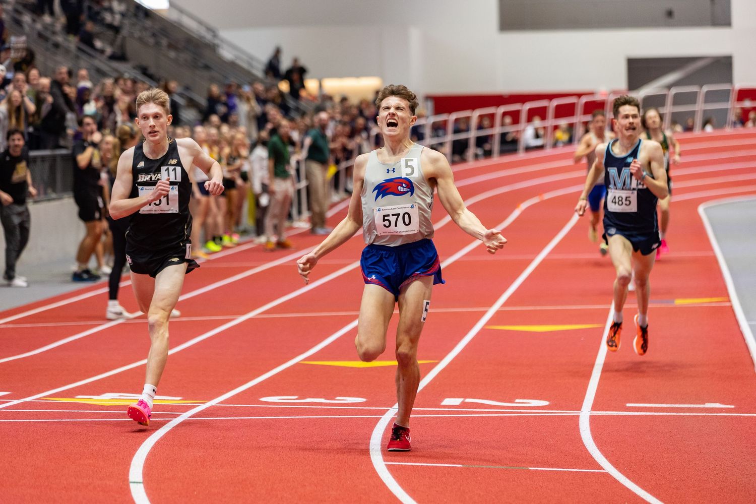 Runners competing in intense indoor track race on red track.