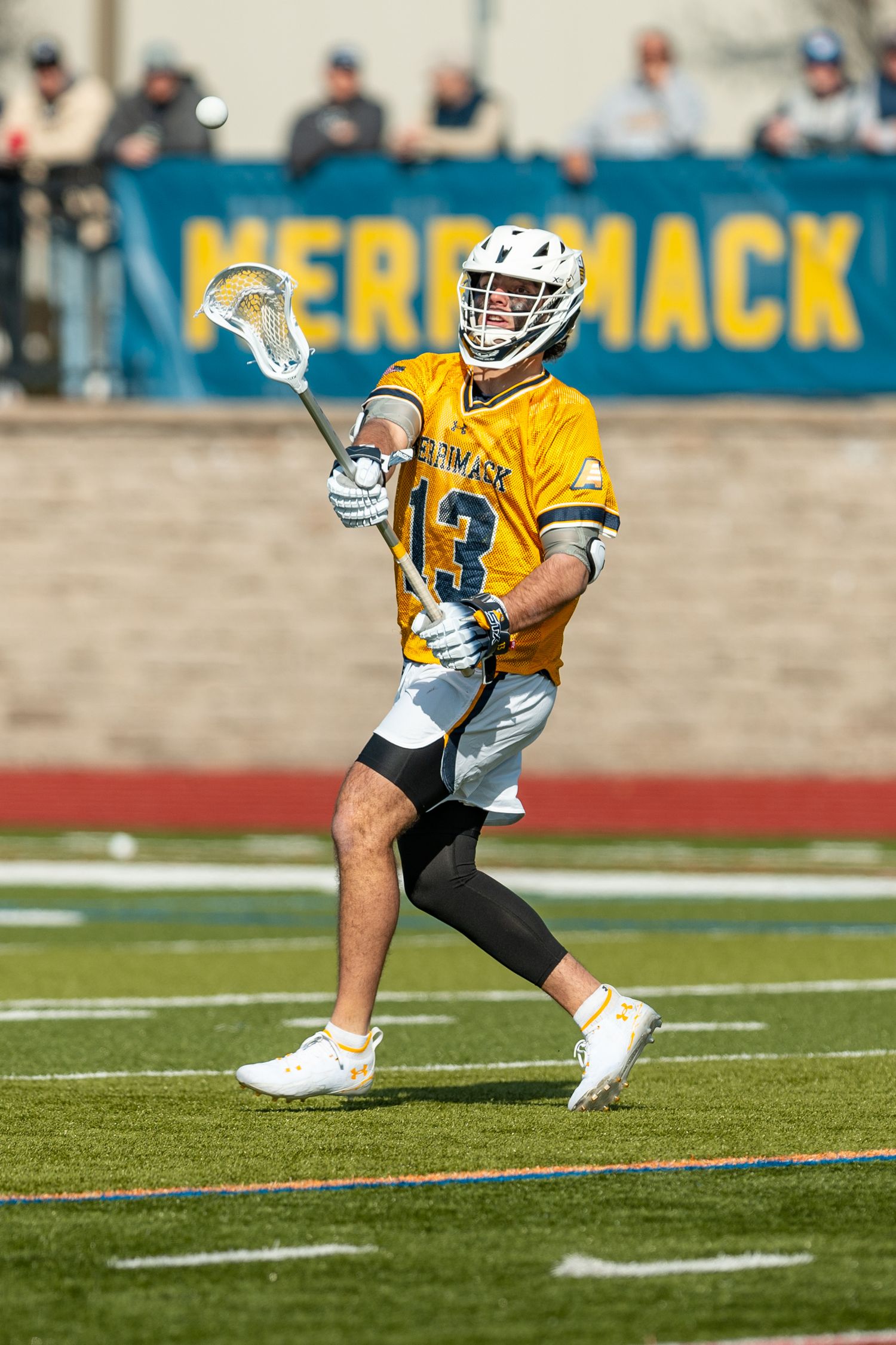 Lacrosse player in yellow jersey carries ball across field during game.