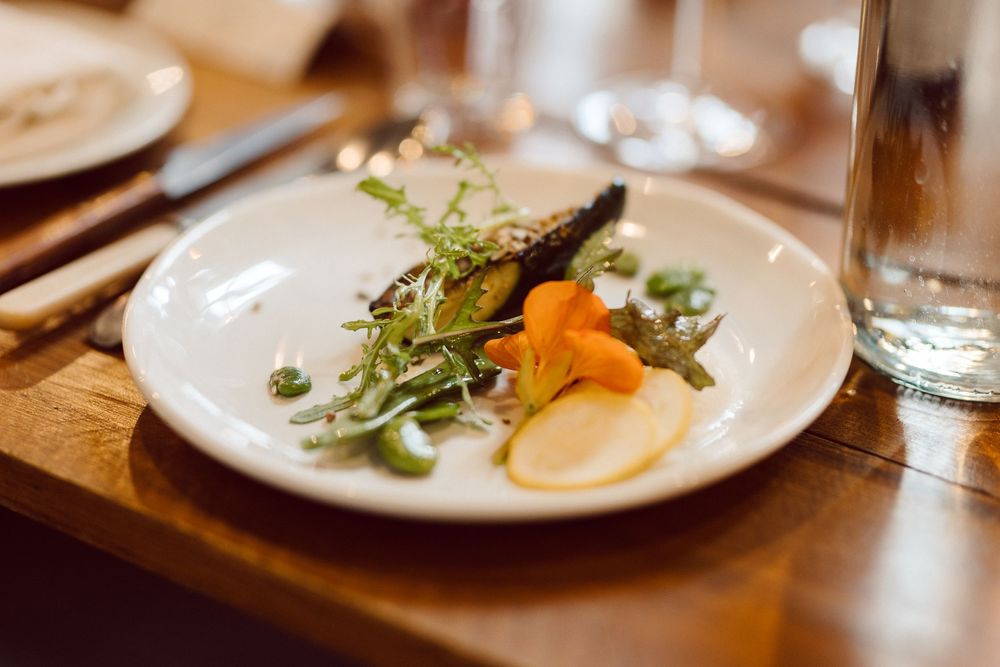 Elegant plated dishes with fresh herbs and garnishes arranged on a wooden restaurant table in warm lighting.