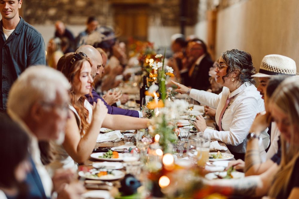 Wedding guests enjoy a candlelit dinner reception at elegantly set tables in a warm, intimate venue.