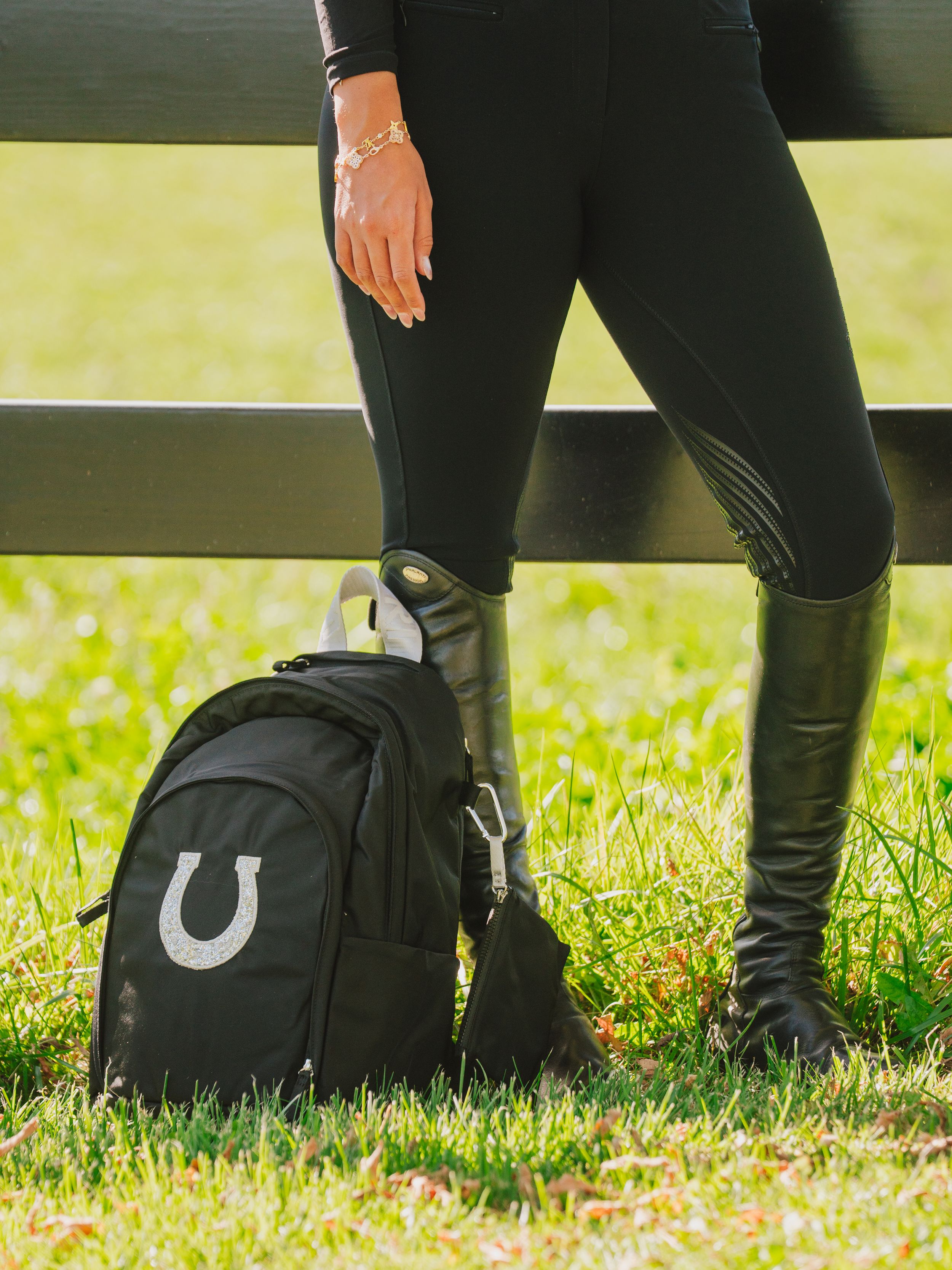 Close-up of black boots and leather pants standing on grass with a backpack visible in the background.
