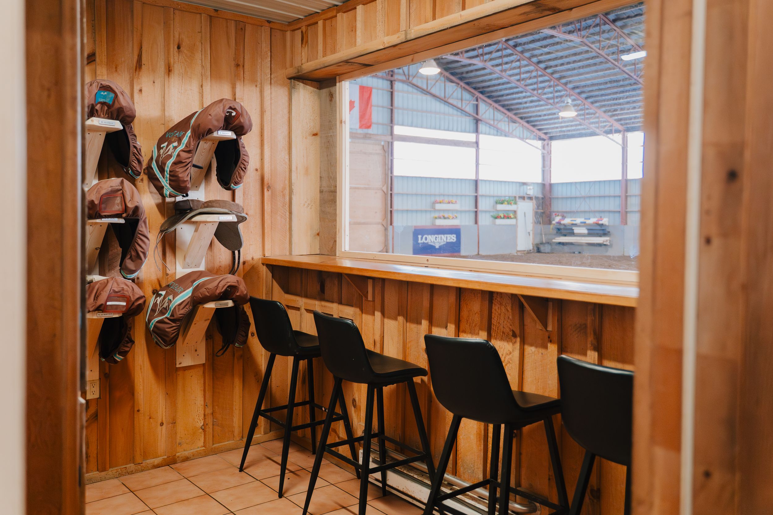 A rustic wood-paneled room with black bar stools and built-in benches along the wall features industrial lighting.