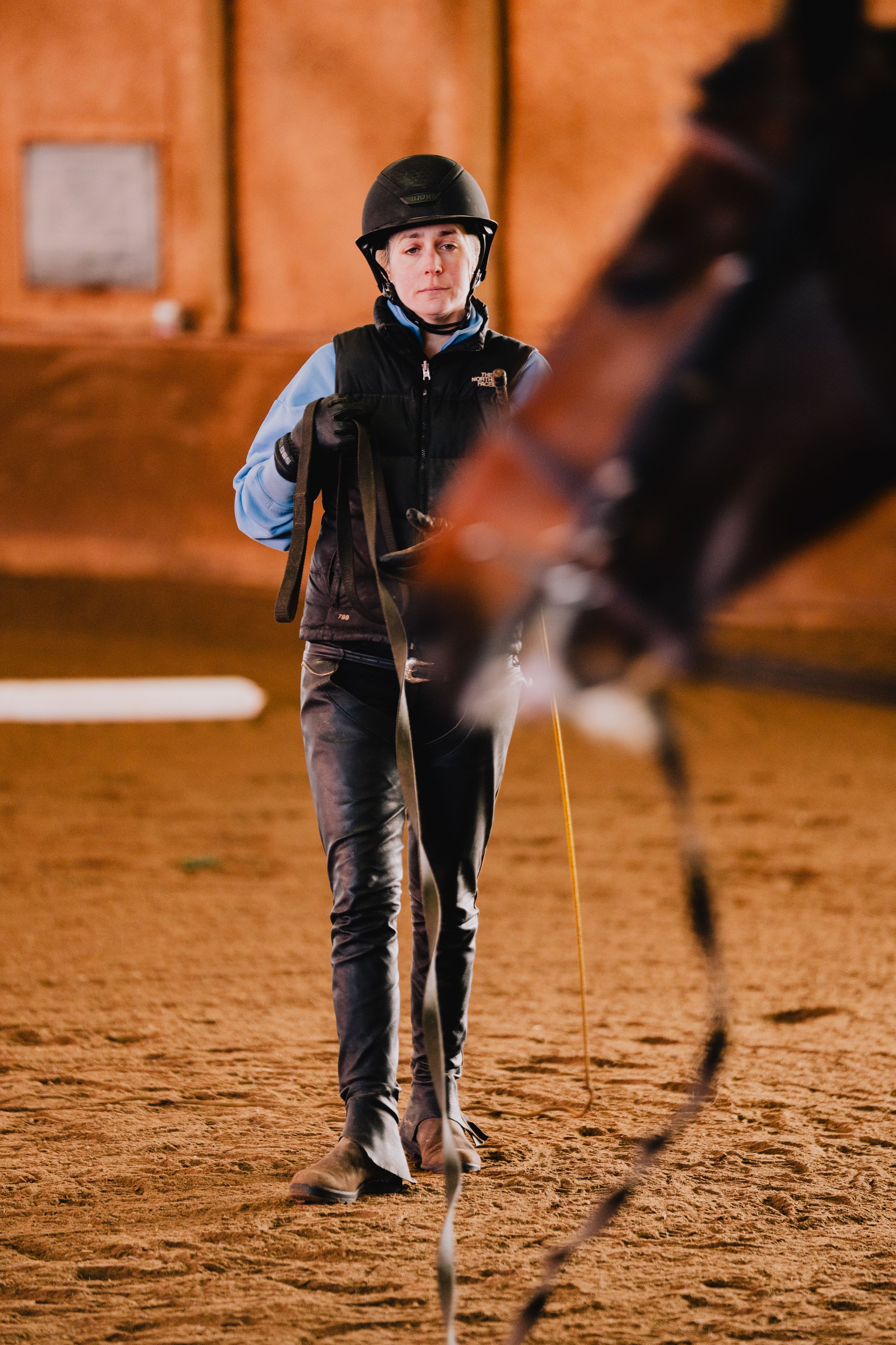 Young equestrian wearing black riding gear and helmet practices in a sandy arena with focused determination.