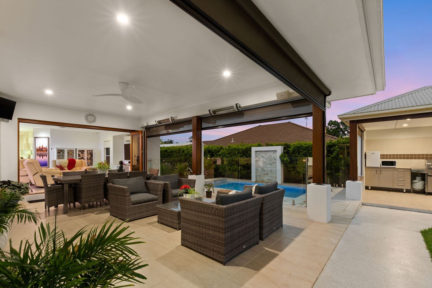 Expansive covered alfresco entertaining area with lounge seating, pool view, and outdoor kitchen at twilight.