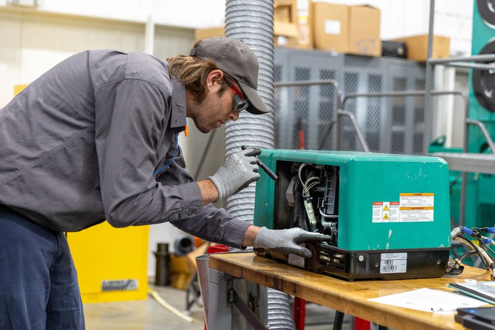 Factory worker operates industrial machinery in manufacturing facility with green equipment and control panels.