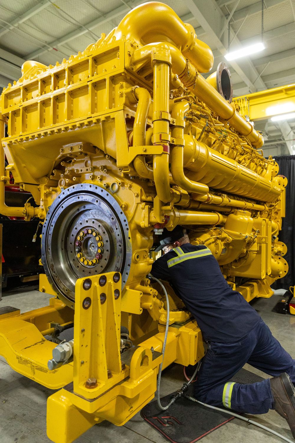 Mechanic working on large yellow industrial diesel engine during maintenance in workshop facility.