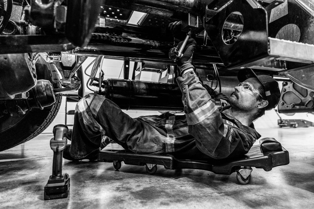 A mechanic lying on a creeper under a vehicle performs maintenance work in black and white photography.