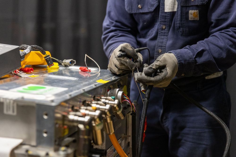 Worker in blue coveralls operates industrial equipment in manufacturing facility.
