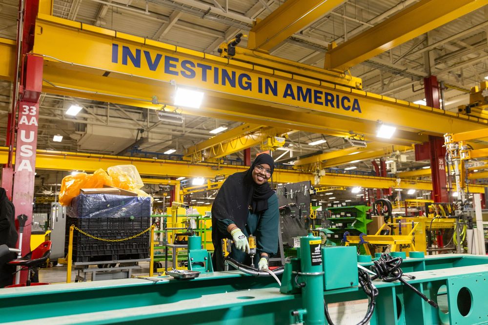 Industrial manufacturing facility with large yellow overhead cranes and turquoise machinery on the production floor.