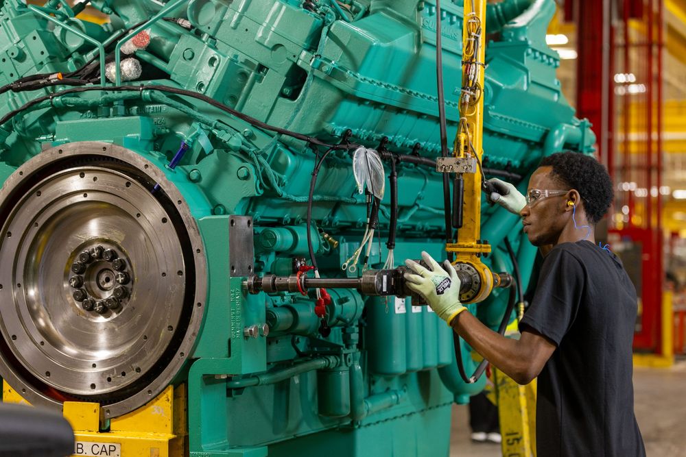Workers inspect and maintain large industrial diesel engines in a manufacturing facility service bay.