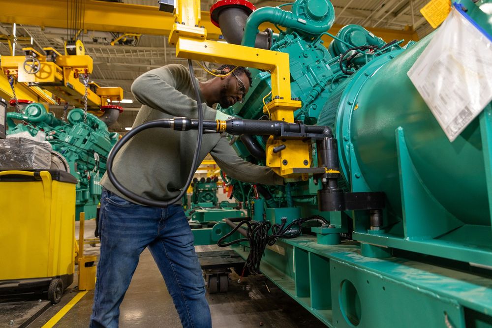 Factory workers performing maintenance on massive turquoise-colored industrial power generators.