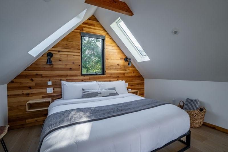 Cozy attic bedroom with wooden paneled walls, skylights, and crisp white bedding in rustic modern style.
