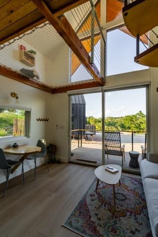 Modern tiny house interior with high ceiling, exposed wooden beams, and large sliding glass doors opening to outdoor deck.