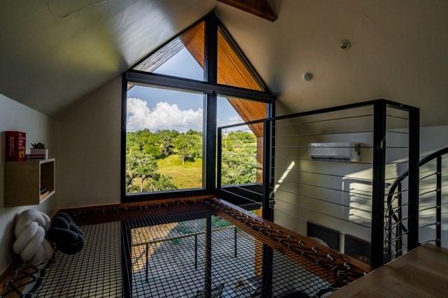 Modern loft interior with large triangular window overlooking green landscape and featuring a suspended net floor.