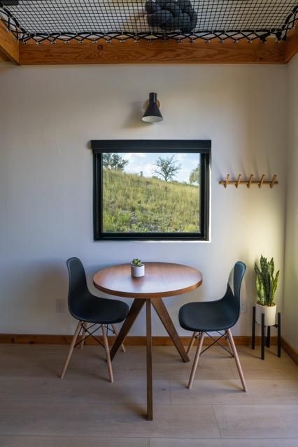 Modern dining area with round wooden table, black chairs, and a panoramic window overlooking nature.