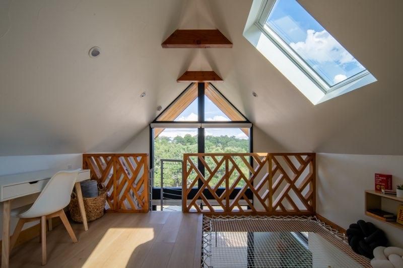 Cozy attic room with skylights, wooden beams, and a balcony overlooking mountain landscapes.