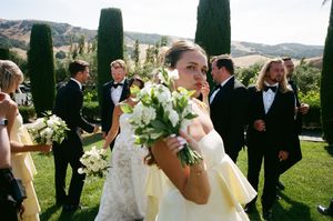 Wedding party gathered outdoors at scenic vineyard venue with tall cypress trees and rolling hills in background.