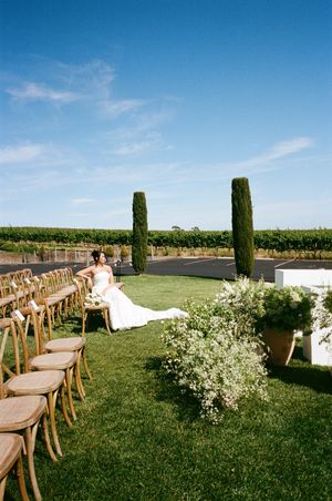 Rustic wooden chairs arranged in rows on a lush green lawn for an outdoor wedding ceremony with white floral decorations.