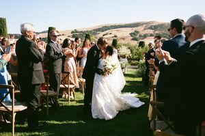 Wedding guests gathered on a scenic lawn with cypress trees and rolling hills in the background.