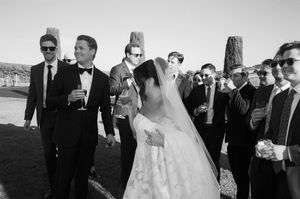 Wedding party members gather outdoors for a candid moment during a celebration on a sunny day.