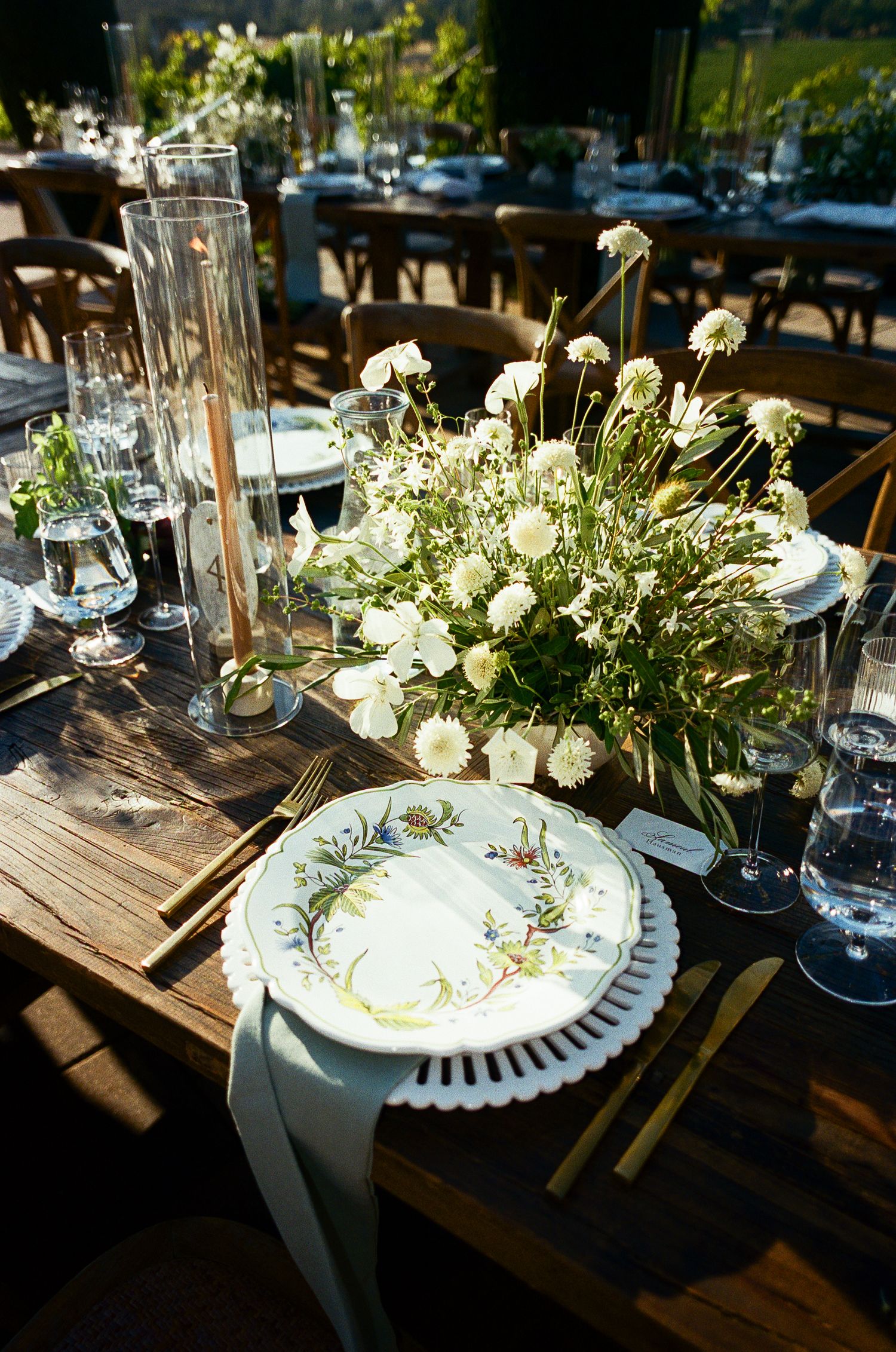 Elegant table settings with white floral centerpieces and rustic wooden tables at an outdoor wedding reception.