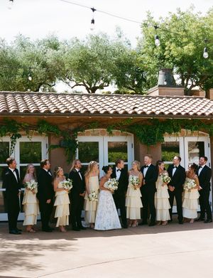 A panoramic view of a wedding party lined up under a covered outdoor walkway with Spanish-style architecture.